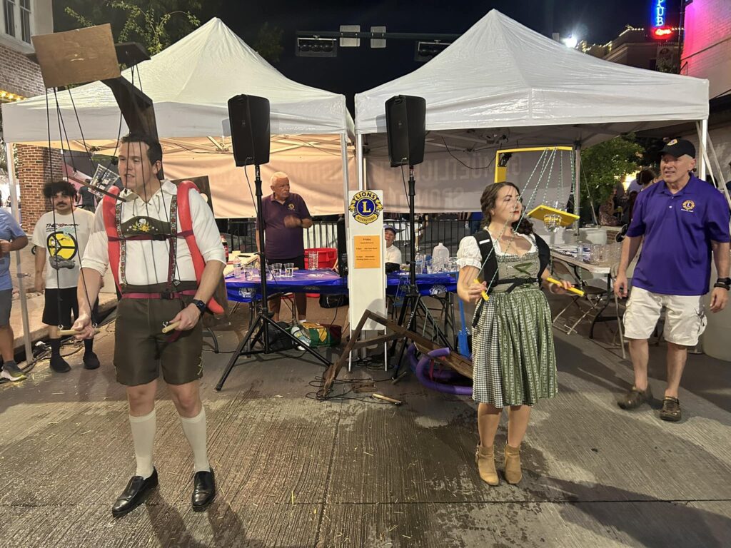 Demonstrating drinking devices in Oktoberfest costumes with the Lions booth in the background